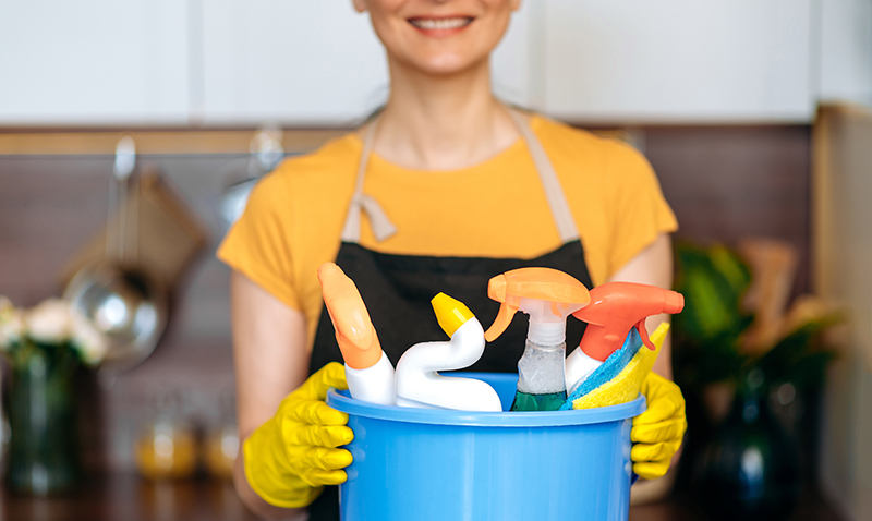 Cleaning service. Close-up of female cleaner hands, stand in the kitchen, holds bucket with detergents and rags, cleaning and cleanliness concept